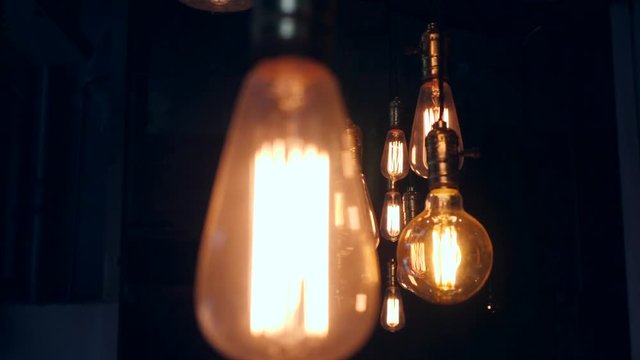Vintage Edison Lamp Lighting Decoration in Loft Style. Old light bulbs Hanging on Ceiling in Restaurant. Light in the dark. 4K.