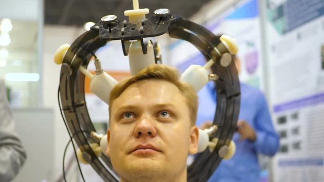 Man wired to an EEG machine or electroencephalograph which produces a graphical record of electrical activity of the brain. Young man set on his head. Electroencephalographic examination