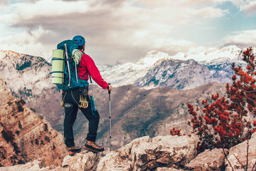 Young mountaineer standing with backpack on top of a mountain and enjoying the view