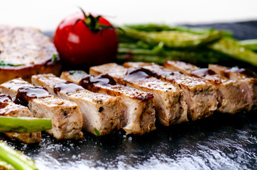 Grilled pork chops, steaks with vegetables, tomatoes, beans and sauce on a black slate. Fresh meat with foam. Dark background. Grilled and barbecue concept. 