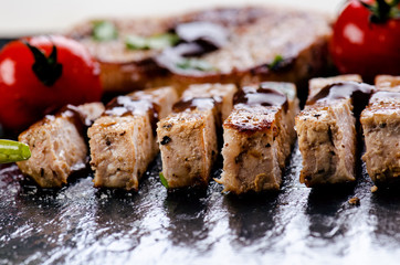 Grilled pork chops, steaks with vegetables, tomatoes, beans and sauce on a black slate. Fresh meat with foam. Dark background. Grilled and barbecue concept. 