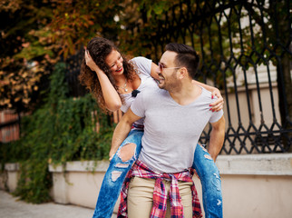 Naklejka premium Attractive young man carrying pretty girlfriend on his back and laughing together.