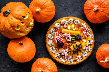 Halloween tradition. Pumpkin pie and pumpkin with scary face on black background top view