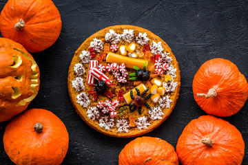 Halloween tradition. Pumpkin pie and pumpkin with scary face on black background top view copyspace