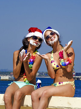 Photo of two young girls in Santa's hats having fun on the beach with shaving foam. Happy Christmas on vacation