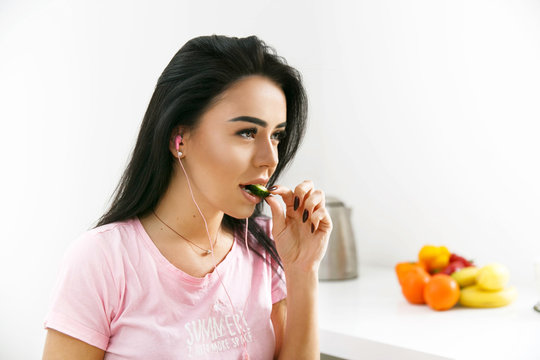 Fit brunette eats cucumber listening to the music in the earphones