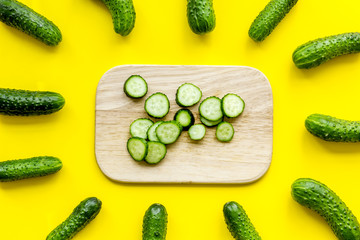 Make salad with fresh cucumbers. Vegetables near desk with sliced cucumbers on yellow background top view