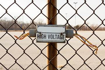 Disconnected electrical junction box with wires hanging on a chain link fence.  High Voltage...