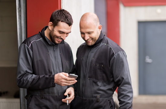 auto mechanics with smartphone at smoking brake