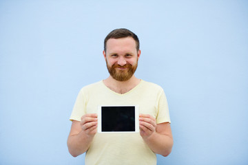 cheerful man with a red beard points at the tablet, space for text