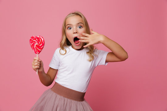 Portrait of a surprised little girl holding heart shaped lollipop