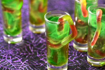 green Halloween jello shots with gummy worms on the purple background