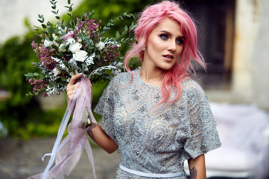 Stunning woman with pink hair stands with large wedding bouquet