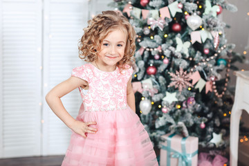 ittle girl in a solemn pink dress is standing near the Christmas tree