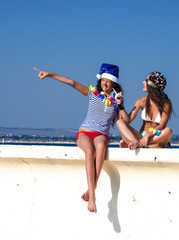 Two girlfriends in a Santa hat and in the image of a pirate during a beach holiday. Christmas, holidays and people concept - friendship and fun