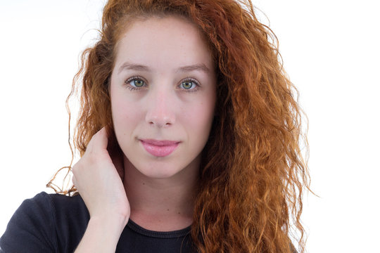 Young woman straightens her hair and looks at the camera. She is redheaded and young. White background. Black shirt..