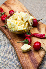 Composition with cheese pieces in olive oil and hot peppers on an olive wood cutting board
