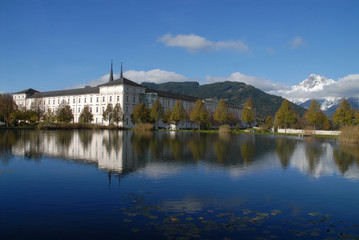 Fototapeta na wymiar Reflection of Admont Abbey (Stift Admont) and mountains with snow on top in a lake