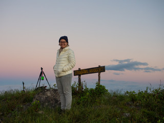 The traveler is standing by tripods and the achievement sign written in Thai which mean I am the conquer of this hill, Doi Phu Wae at Nan, Thailand