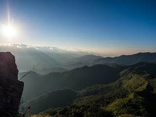 The morning sunrise behind the mountain cliff shine brightly through the white cloudy sky, the shade of them dropped on the green mountain range of Doi Phu Wae in Nan province Thailand