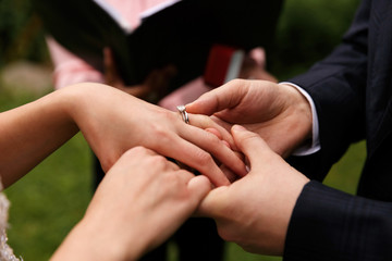 Obraz na płótnie Canvas Groom puts wedding ring on bride's finger