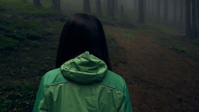 Back View Of A Young Woman Hiking In Forest. Hiking Woman Walking In Gloomy Mystical Forest - Thriller Scene. Wide-angle Lens. Close-up
