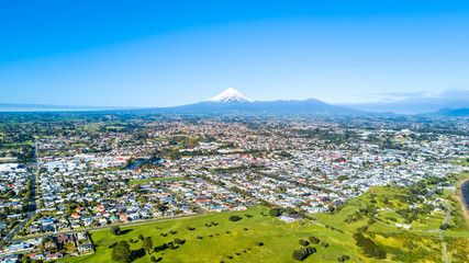 Aerial view on a New Plymouth residential suburb surrounded by green meadow with Mount Taranaki on the background. New Zealand