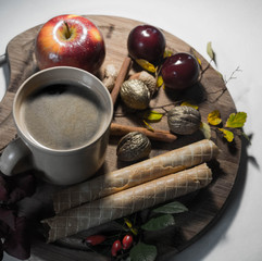 autumn coffe drink with waffers, apple and cinnamon and autumn leaves on wooden plank against white background