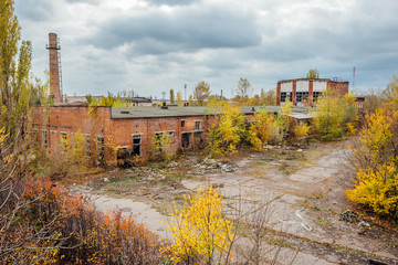 Fototapeta na wymiar Old obsolete ruined overgrown concrete industrial buildings in autumn. Abandoned factory 