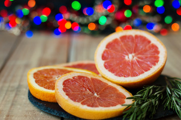 Fototapeta na wymiar Sliced orange and grapefruit served with fresh rosemary on black slate board, blurred lights as background