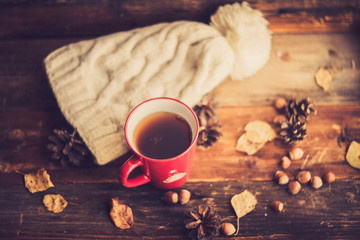 Mug of hot coffee in a woman's hand in a sweater in the autumn setting on a wooden table with a knitted scarf, sweater. Comfort, warmth, cozy