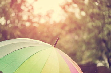 Close up umbrella in rainbow colors in rainy autumn day, blur focus. Instagram warm filter