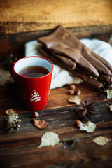 Hands in red knitted gloves holding a hot cup of coffee against yellow leaves background. Concept of autumn time, warmth and coziness