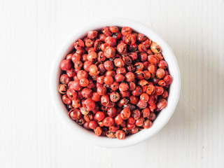 Pile with dried pink pepper berries on white wooden table. Close up view of pink peppercorn. Top view or flat-lay.