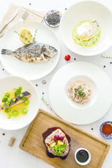 a lot of fish dishes on white table. Top view