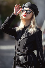 Obraz na płótnie Canvas Fashion woman in black leather cap, trendy glasses and red lips. Stylish look in fashion coat outside. Autumn look.