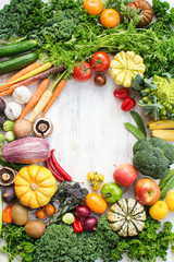 Colorful frame made of fresh raw vegetables, fruits herbs on white wooden background, copy space for text in the middle, top view, selective focus