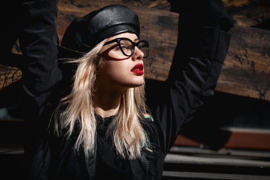 High fashion close up portrait of sexy blong woman in leather cap and provocative red lips over wooden background.