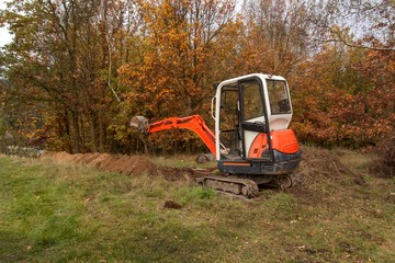 Mini excavator on construction site. Construction of a family house near a forest.
