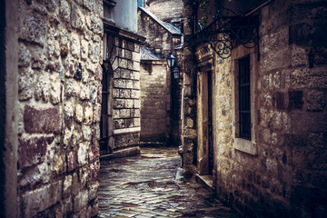Dark vintage medieval narrow winding street with ancient stone building facade with medieval...