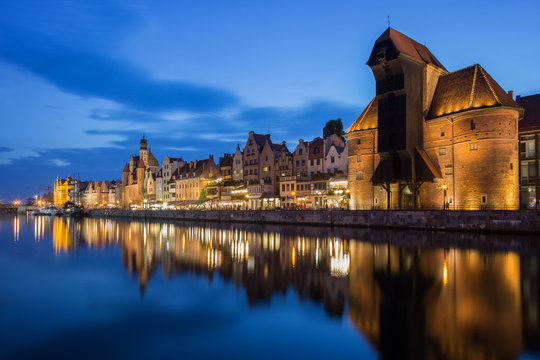 Scenic view of the lit Crane and other old buildings along the Long Bridge waterfront at the Main Town in Gdansk, Poland, in the evening.