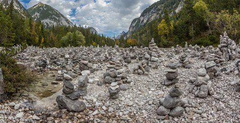 Stone figures (multiple) in a riverbed in the mountains. Cloudy sky, autumn.