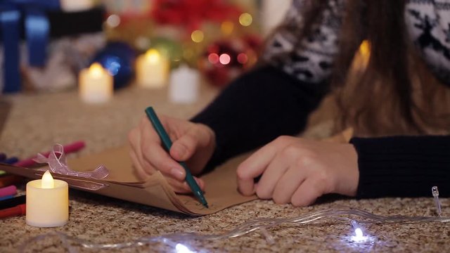 Handles of the little girl draw a picture. a teenage girl lying on the floor, drawing a drawing for Santa Claus near a beautifully dressed Christmas tree. Close-up.