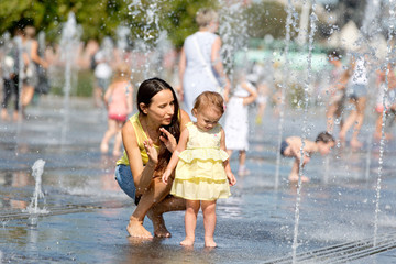 Mother and child playing with water jets of the fountain on a hot summer day 