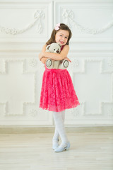 smiling beautiful baby girl in a red dress on a light background in an embrace with a small soft toy