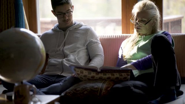 Homeschooling teenage boy and mother discuss art history with a globe of the world in front of them for reference in a relaxed living room atmosphere.