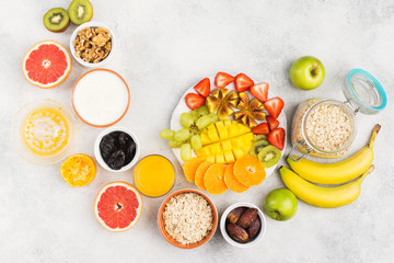 Healthy breakfast with oats, variety of fruits, strawberries, mango, grapes, figs, bananas and dates, yogurt and nuts served on the white table, top view, copy space for text, selective focus