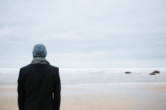Man standing alone on the beach looking out to sea