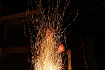 Sparks of a bright fire against the background of a black night. Silhouette of the canting man behind the fires of a bright flame. The witch conjures at the fire at night.