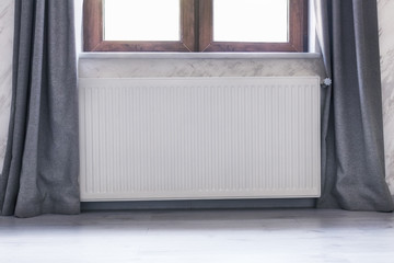 Heating radiator under the window with a wooden frame and curtains.